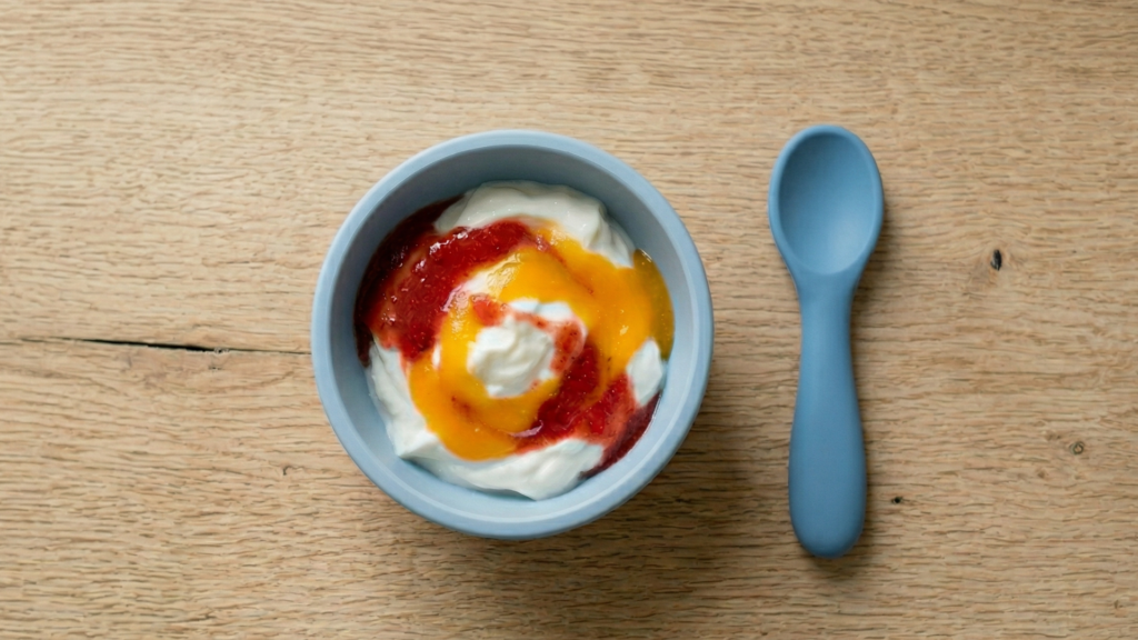 ék balatálban natúr joghurt epres és mangós gyümölcspürével, mellette kék babás szilikon kanál