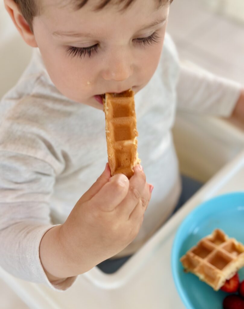 Kisgyerek kézben tartja és eszi a hosszában vágott baba gofrit