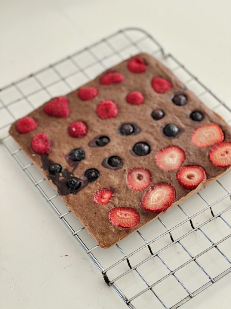 Cukormentes brownie teljes lap hűlőrácson sütés után, tetején málna, áfonya és eperszelet