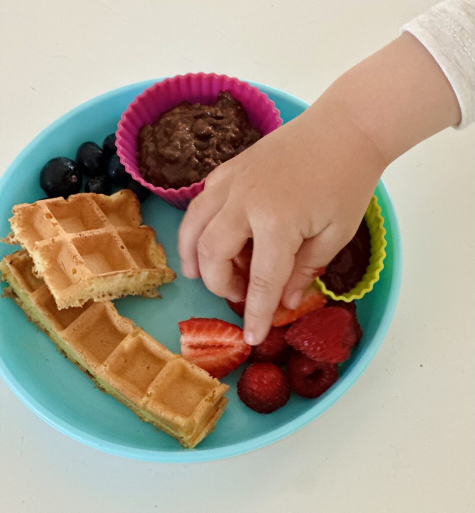 Kisgyerek keze nyúl az epres gofris tányér felé