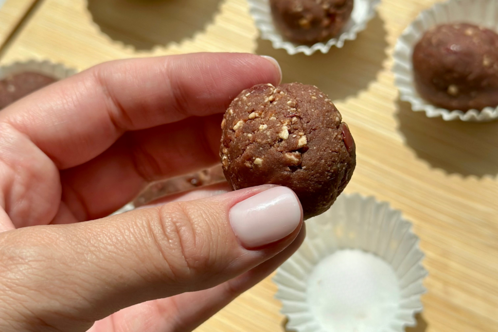 Meggyes-kekszes energiagolyó kézben tartva, háttérben további golyók muffinpapírban