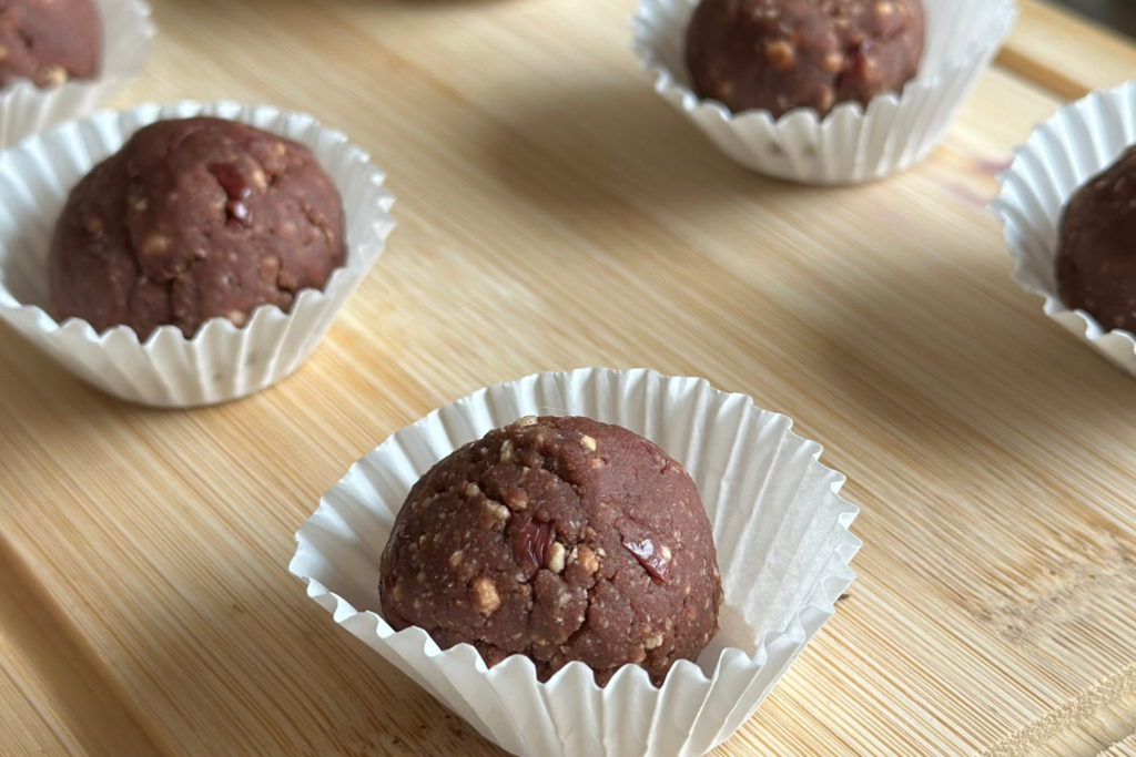 Sötétbarna meggyes-kekszes energiagolyók mini muffinpapírban fatányéron
