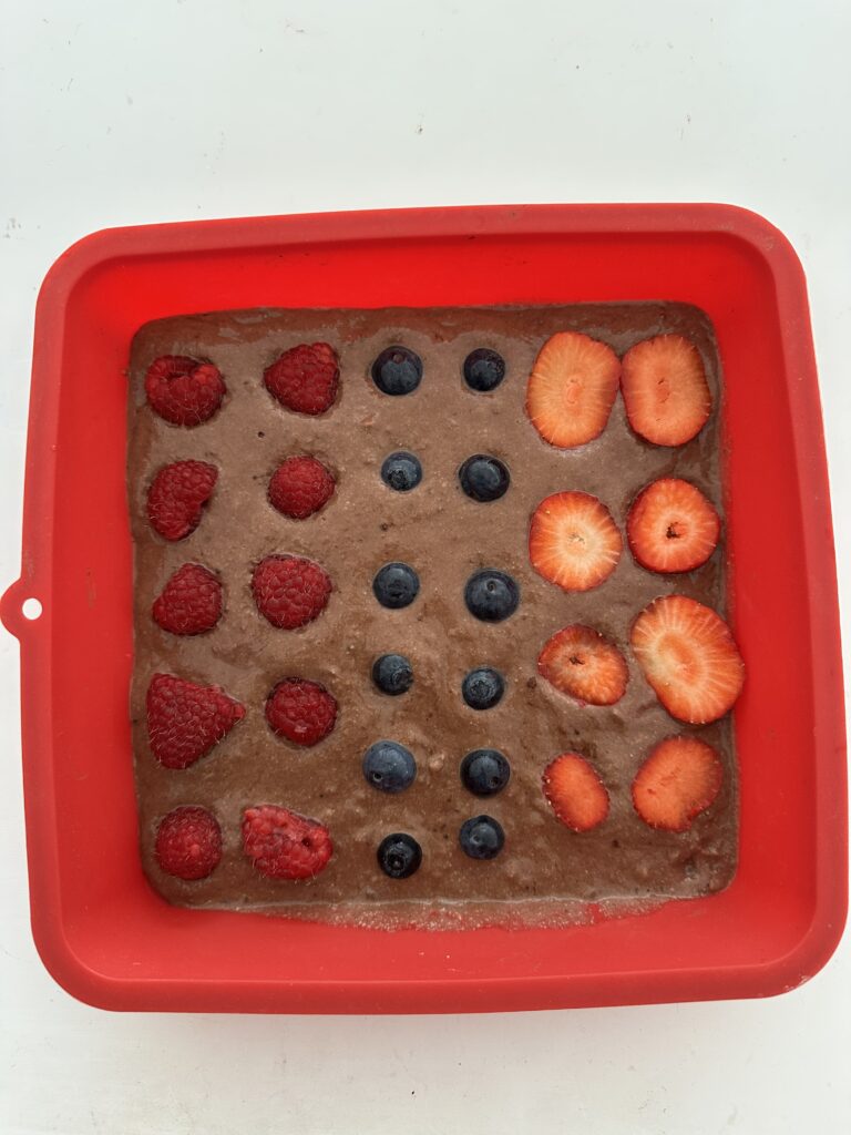 Cukormentes brownie tészta piros szilikon formában sütés előtt, tetején málna, áfonya és eperszelet