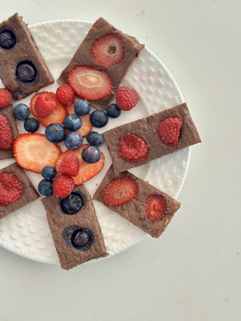 Cukormentes brownie gyümölcsös szeletek fehér tányéron közelről, eperrel és málnával a tetején