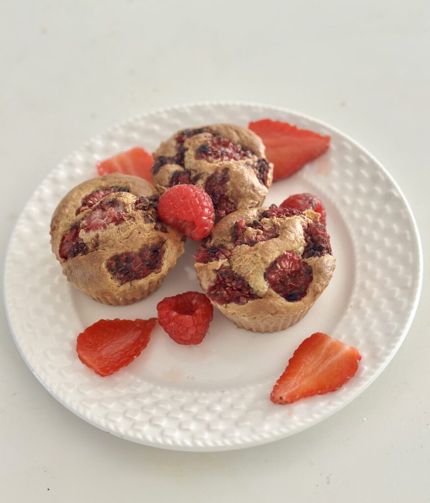 Cukormentes epres-málnás baba muffin fehér tányéron, friss eper- és málnaszeletekkel körítve
