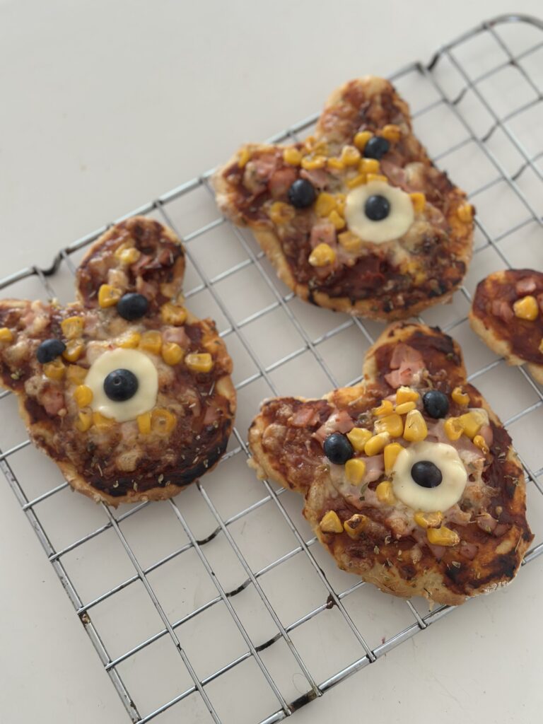 Kész maci mini baba pizzák hűlőrácson, áfonya szemekkel és sajt koronggal díszítve