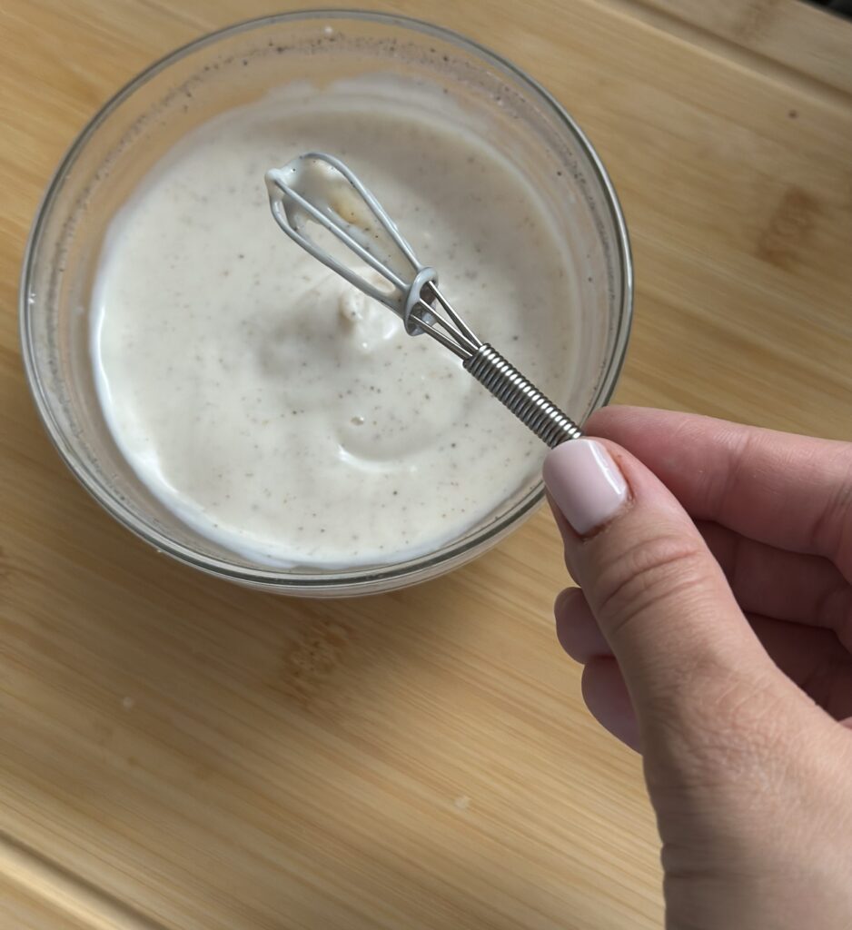 Házi készítésű vaníliás puding üvegtálban kézi habverővel, fahéjas csiga mellé kínálva babáknak és kisgyermekeknek.